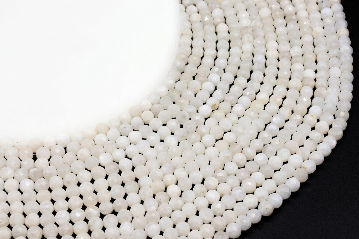 Fils de perles rondes facettées en Pierre de Lune blanche disposés en cercle sur fond noir