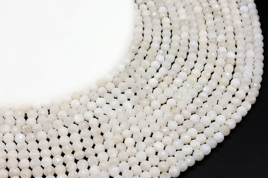 Fils de perles rondes facettées en Pierre de Lune blanche disposés en cercle sur fond noir