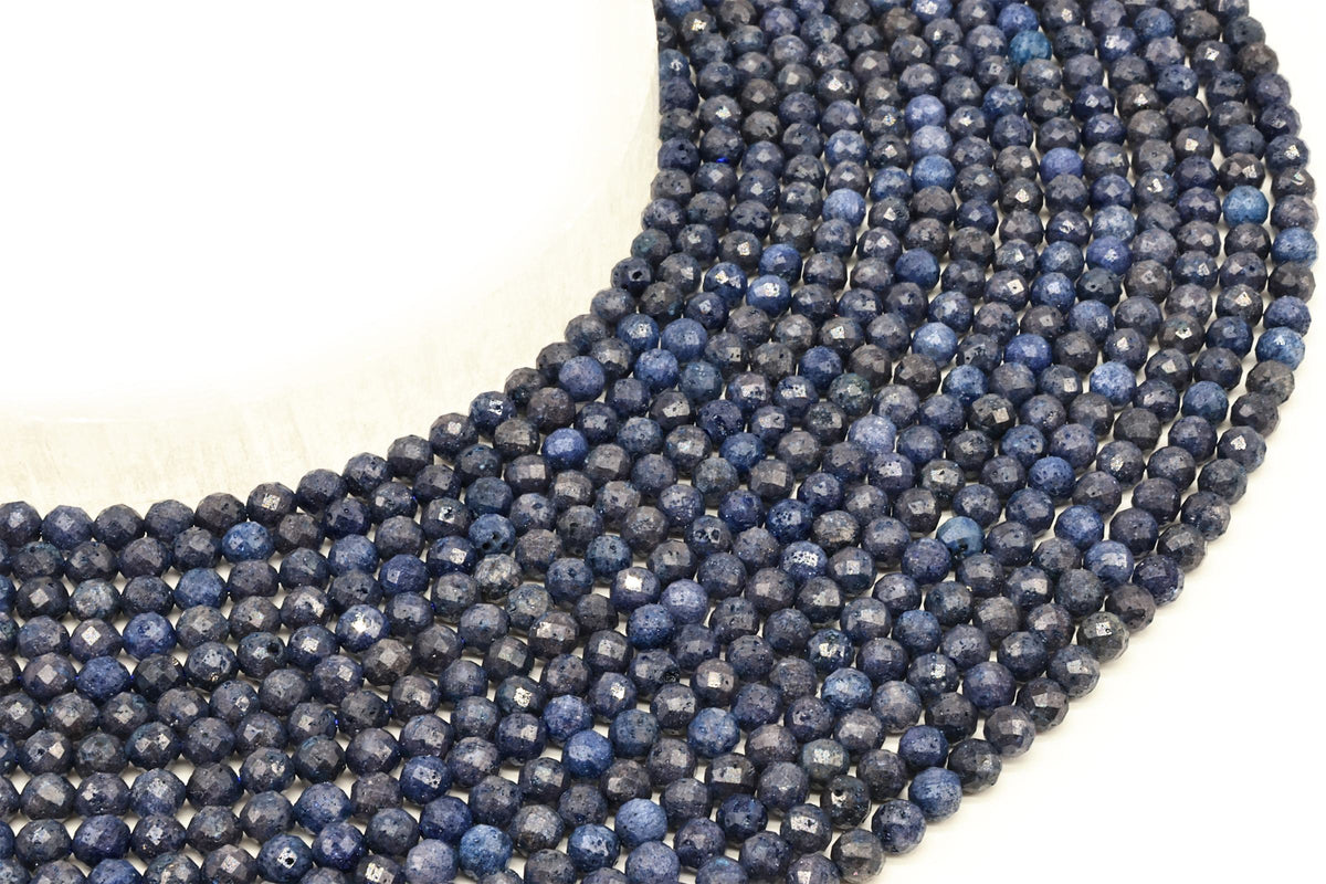 Fils de perles rondes facettées de saphir bleu foncé disposés en arc sur fond blanc