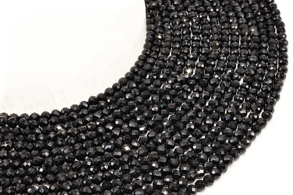 Fils de perles rondes facettées en tourmaline noire alignés sur fond blanc