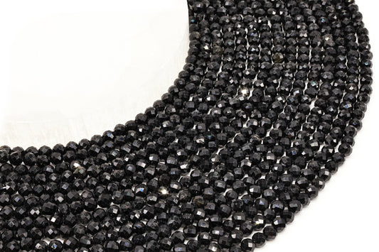 Fils de perles rondes facettées en tourmaline noire alignés sur fond blanc