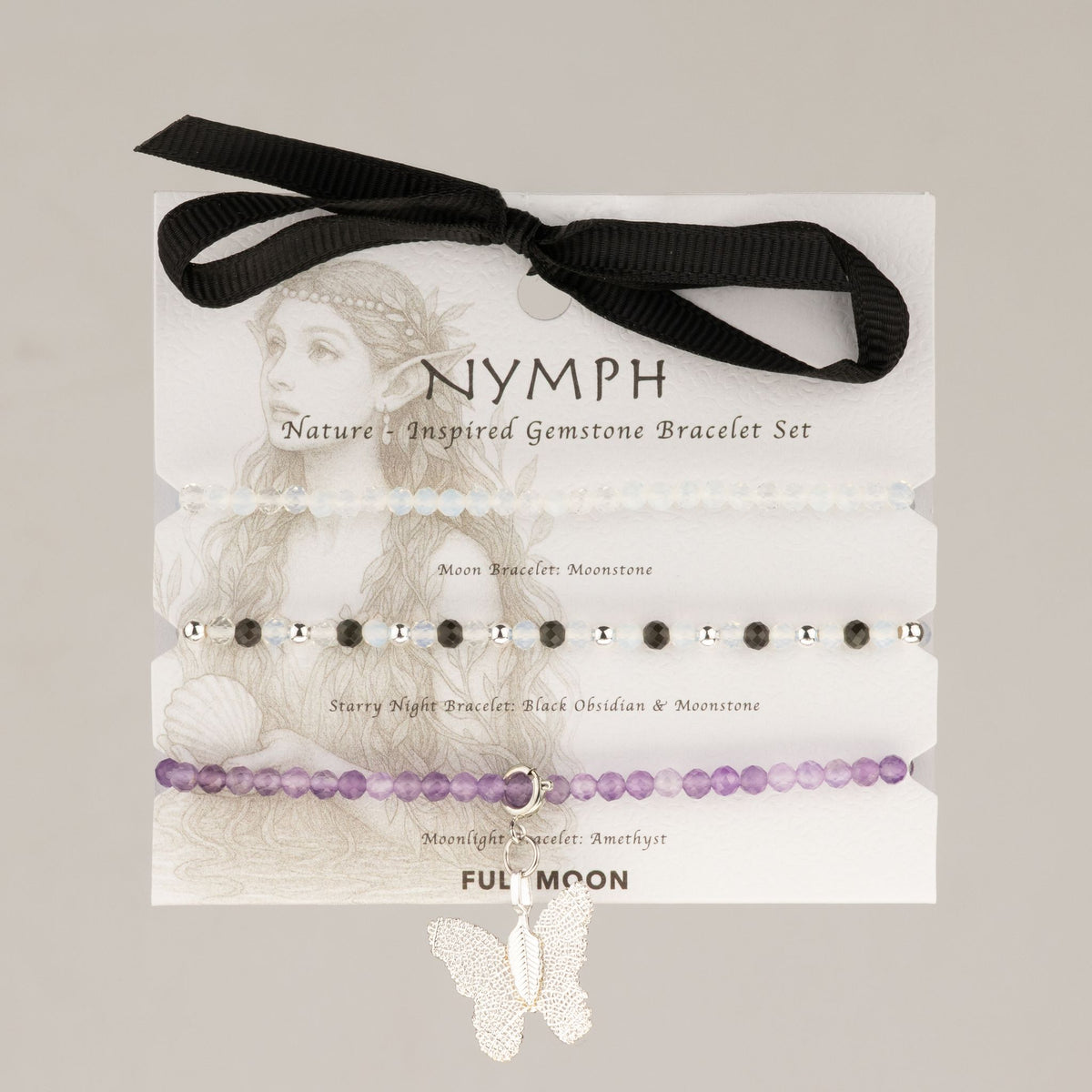 Trois bracelets en perles blanches, noires et violettes avec breloque papillon argentée sur carte illustrée