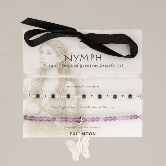 Trois bracelets en perles blanches, noires et violettes avec breloque papillon argentée sur carte illustrée