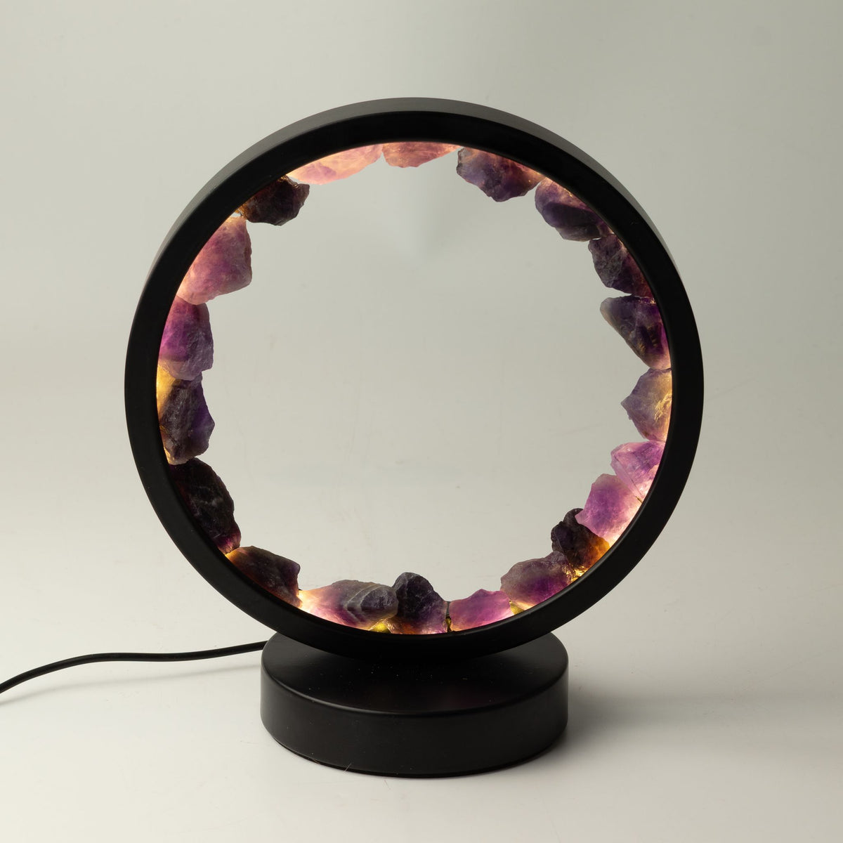 Lampe halo circulaire noire ornée d'un anneau d'améthystes brutes illuminées sur socle
