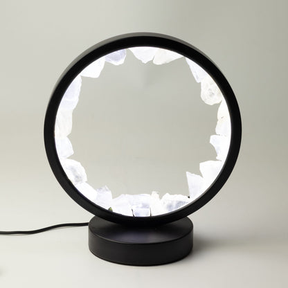 Lampe circulaire noire allumée, bordée de morceaux bruts de cristal de roche