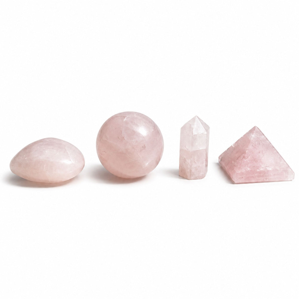 Quatre pierres en quartz rose : cœur, sphère, obélisque et pyramide sur fond blanc