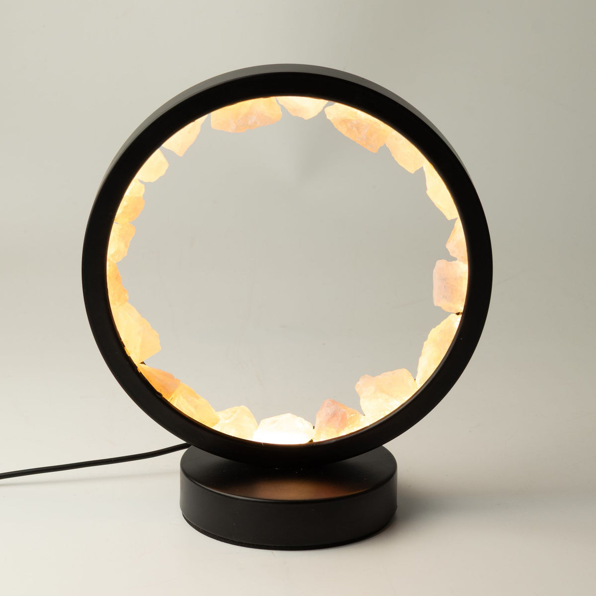 Lampe halo ronde en métal noir sertie de morceaux de quartz rose brut allumée